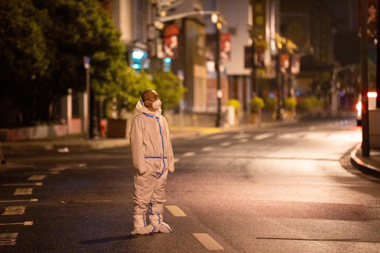 Ein Mann steht in Schutzkleidung auf einer menschenleeren Straße nachts in Schanghai und patrouilliert. 