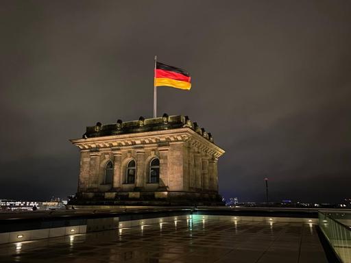 Die Deutschlandfahne auf dem Dach des Reichstages bei Nacht.