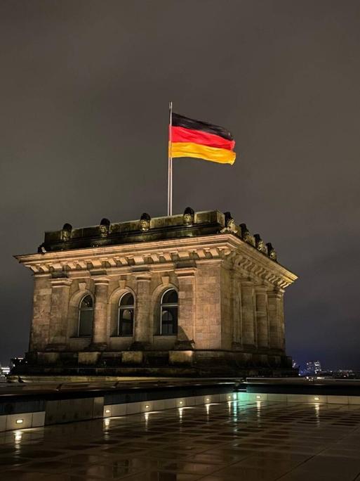 Die Deutschlandfahne auf dem Dach des Reichstages bei Nacht.