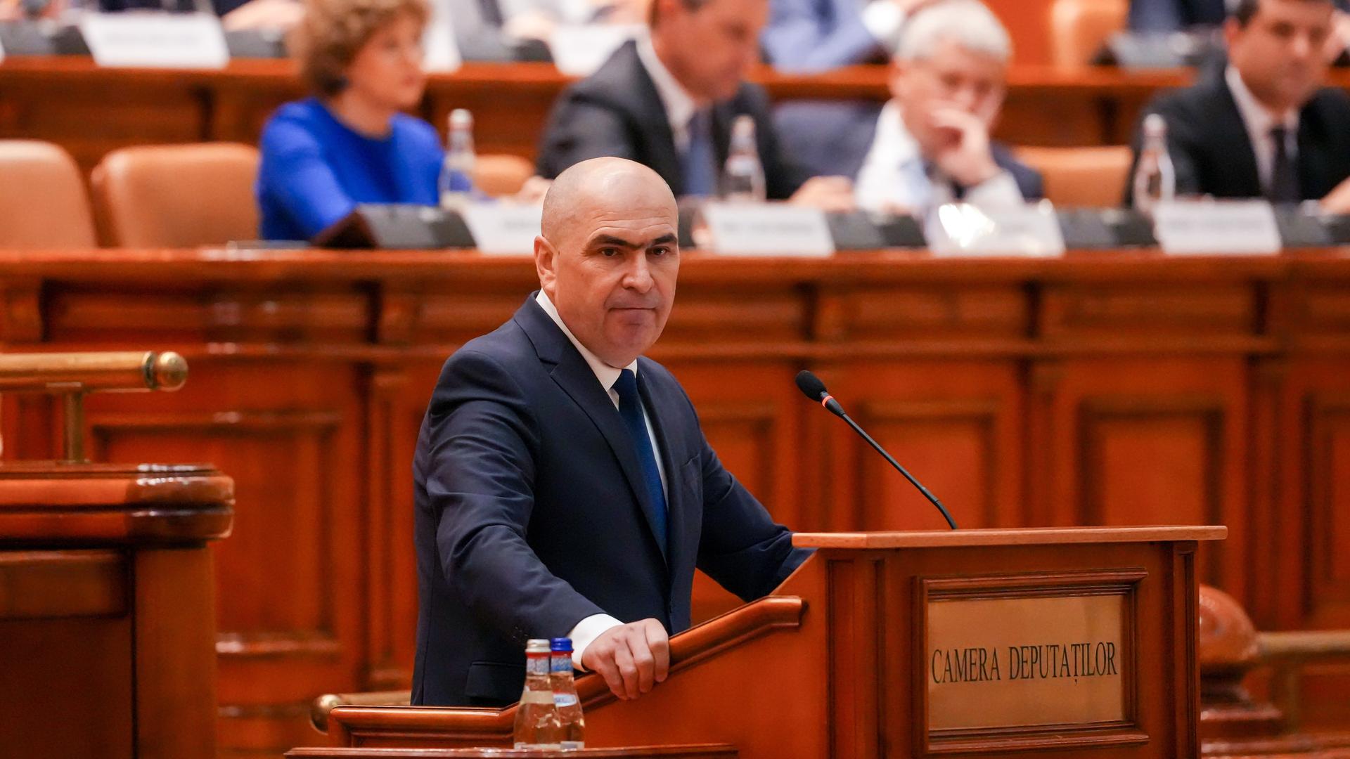 Der rumänische Premierminister Ilie Bolojan spricht in Bukarest (Rumänien) vor einer Parlamentssitzung. Hinter ihm sitzen mehrere Personen. 