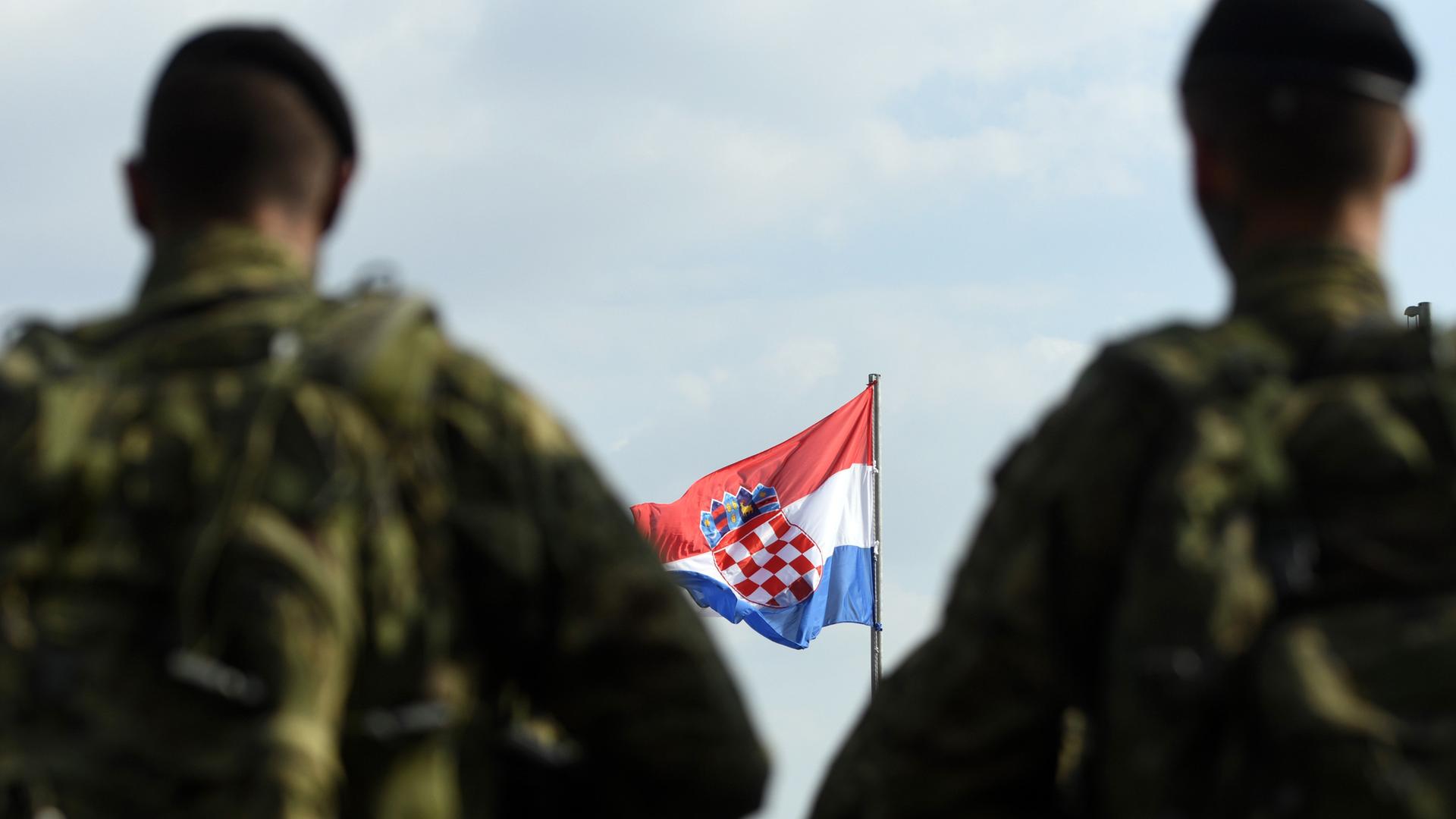 Zwei kroatische Soldaten sind von hinten verschwommen fotografiert. Vor ihnen weht die Flagge Kroatiens. 