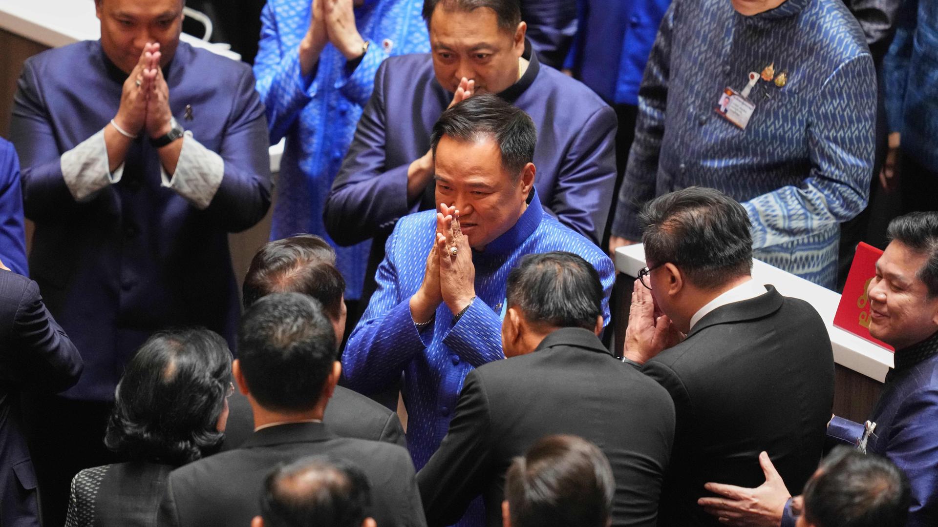 Anutin steht im Parlament zwischen den Abgeordneten und hat die Hände zum Dank vor dem Gesicht gefaltet.