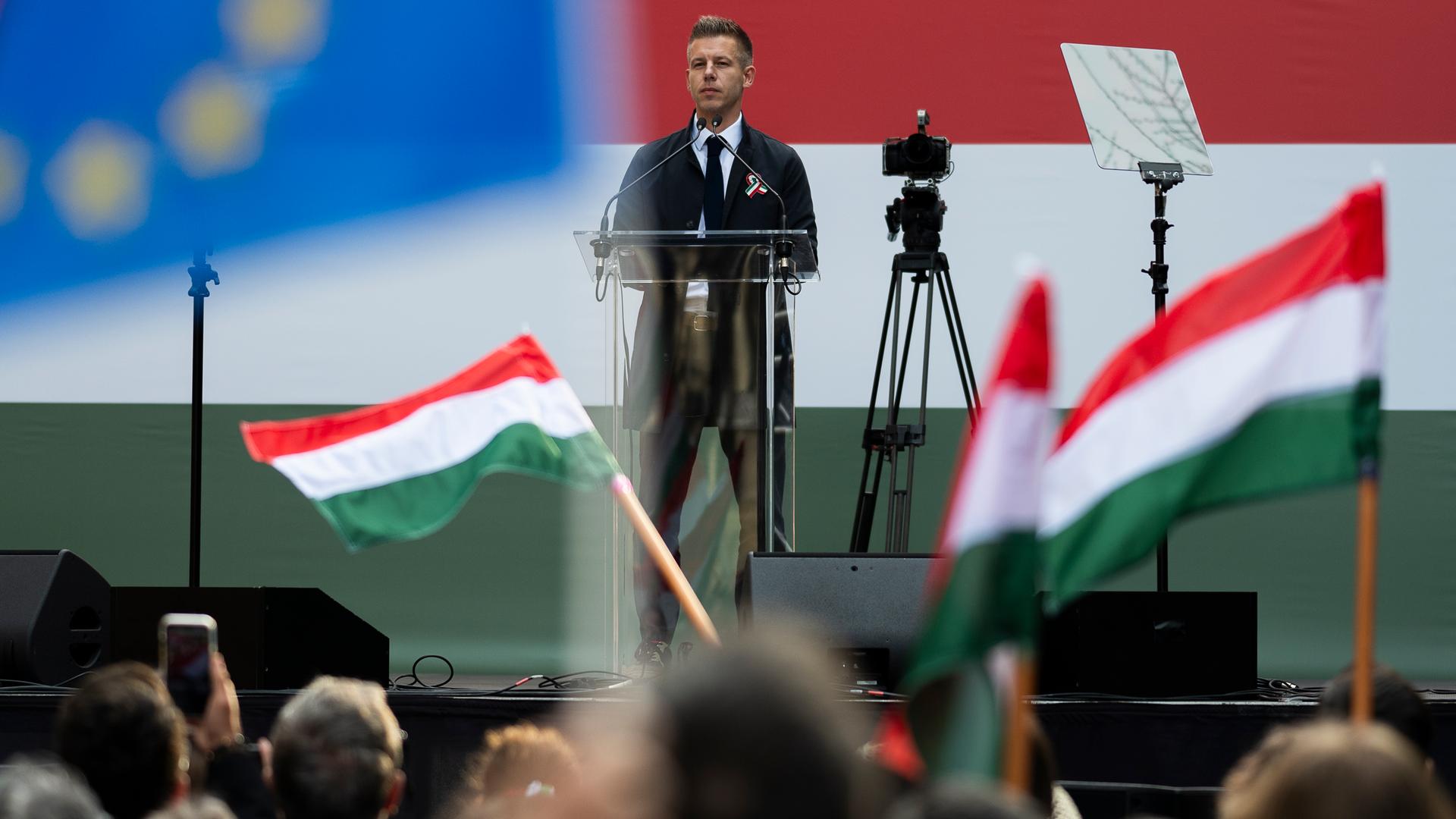 Der ungarische Oppositionspolitiker Magyar redet auf einer Bühne. Davor stehen Demonstranten mit Fahnen.