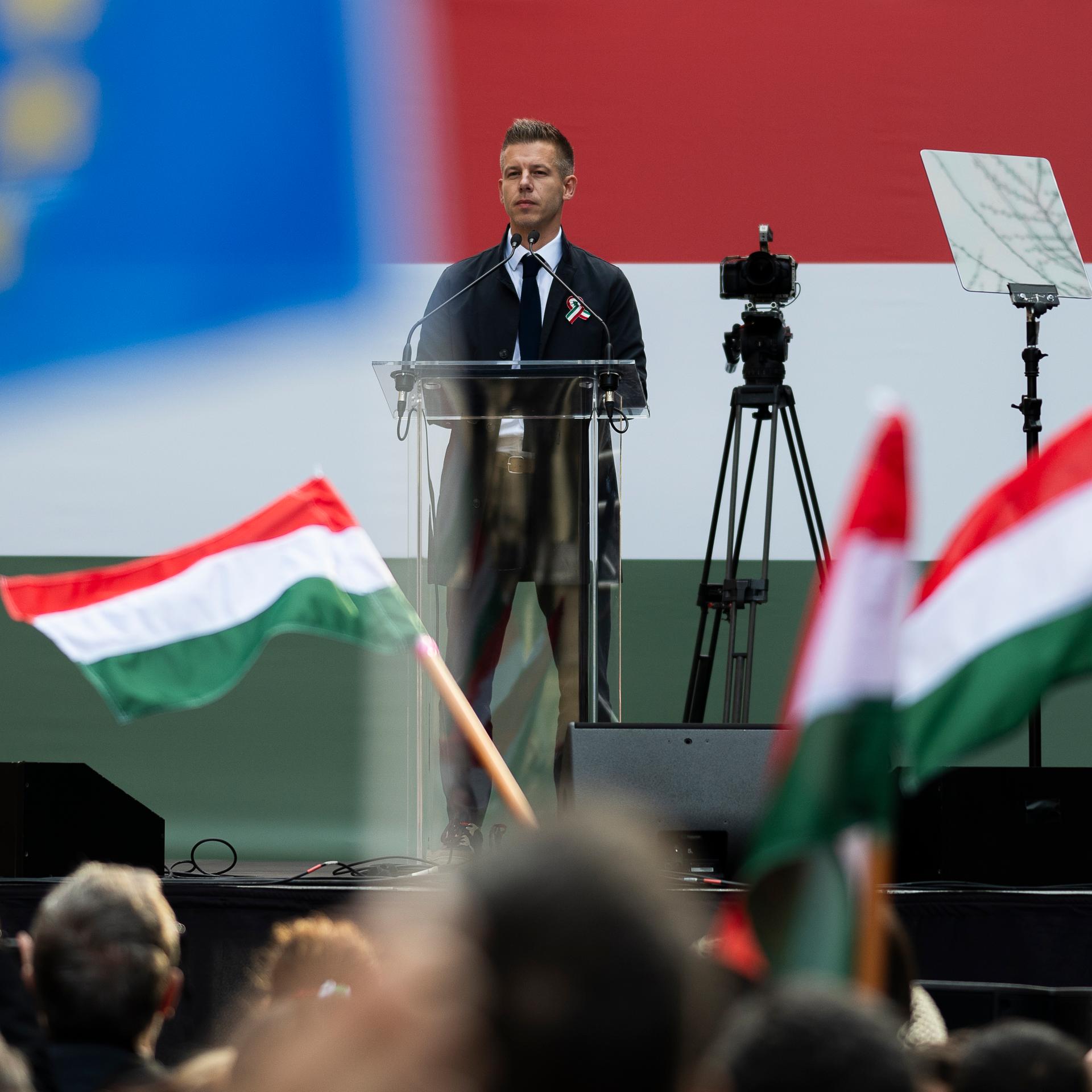 Der ungarische Oppositionspolitiker Magyar redet auf einer Bühne. Davor stehen Demonstranten mit Fahnen.