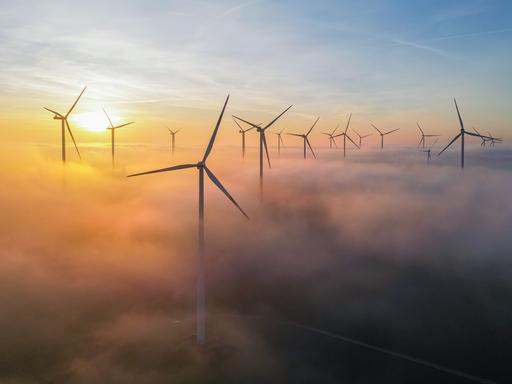 Die Morgensonne leuchtet über dem Nebel zwischen Windenergieanlagen im östlichen Brandenburg (Luftaufnahme mit einer Drohne).