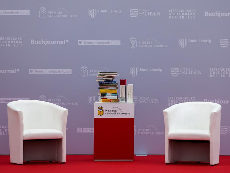 Zwei Sessel und ein Büchertisch stehen am Rande der Verleihung des Preises der Leipziger Buchmesse 2022 in der Glashalle der Messe.