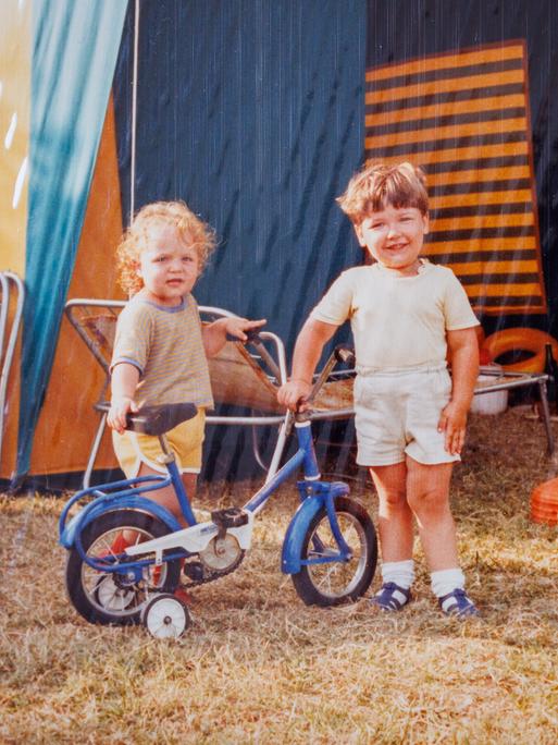 Zwei Kinder posieren während eines Feriencamps in den 1980er-Jahren. Im Hintergrund allerhand Campingequipment.