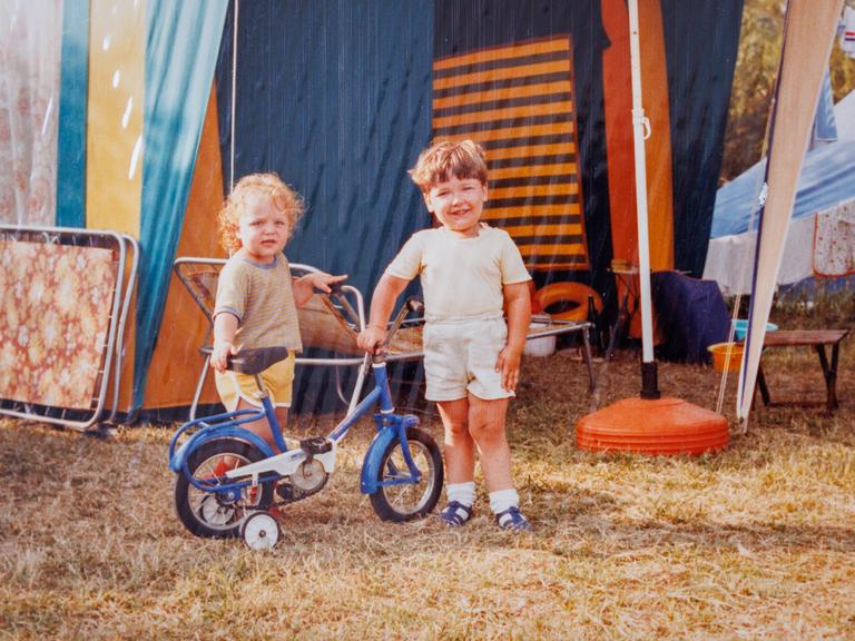 Zwei Kinder posieren während eines Feriencamps in den 1980er-Jahren. Im Hintergrund allerhand Campingequipment.