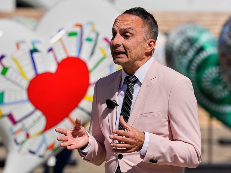 Der ESC-Experte Dean Vuletic gibt in der ESC-Woche am 16.5.2025 in Basel ein Interview. Im Hintergrung ist eine Deko mit bunten Herzen zu sehen.