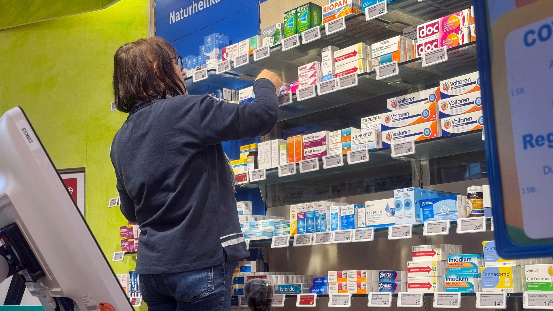 Eine Frau füllt ein Medikamentenregal in einer Apotheke auf.