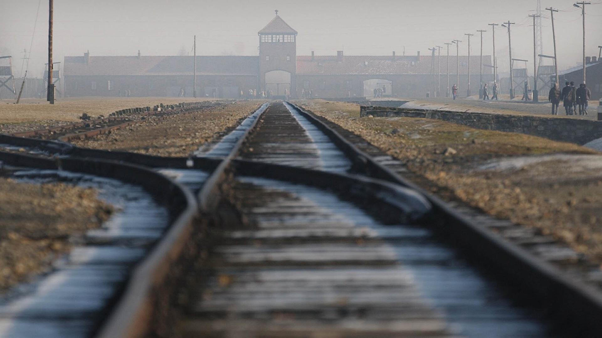 Stillgelegte Bahnschienen führen auf das Hauptgebäude von Auschwitz-Birkenau zu. Das Gebäude liegt im Nebel.