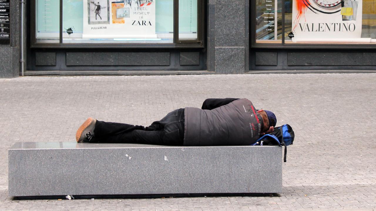 Ein obdachloser Mann schläft auf einem Granitblock in der Fußgängerzone.