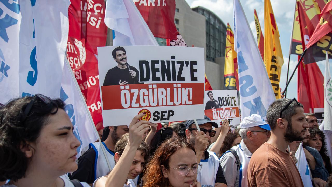 Viele Menschen stehen auf einem Platz, sie halten Schilder und Banner hoch.