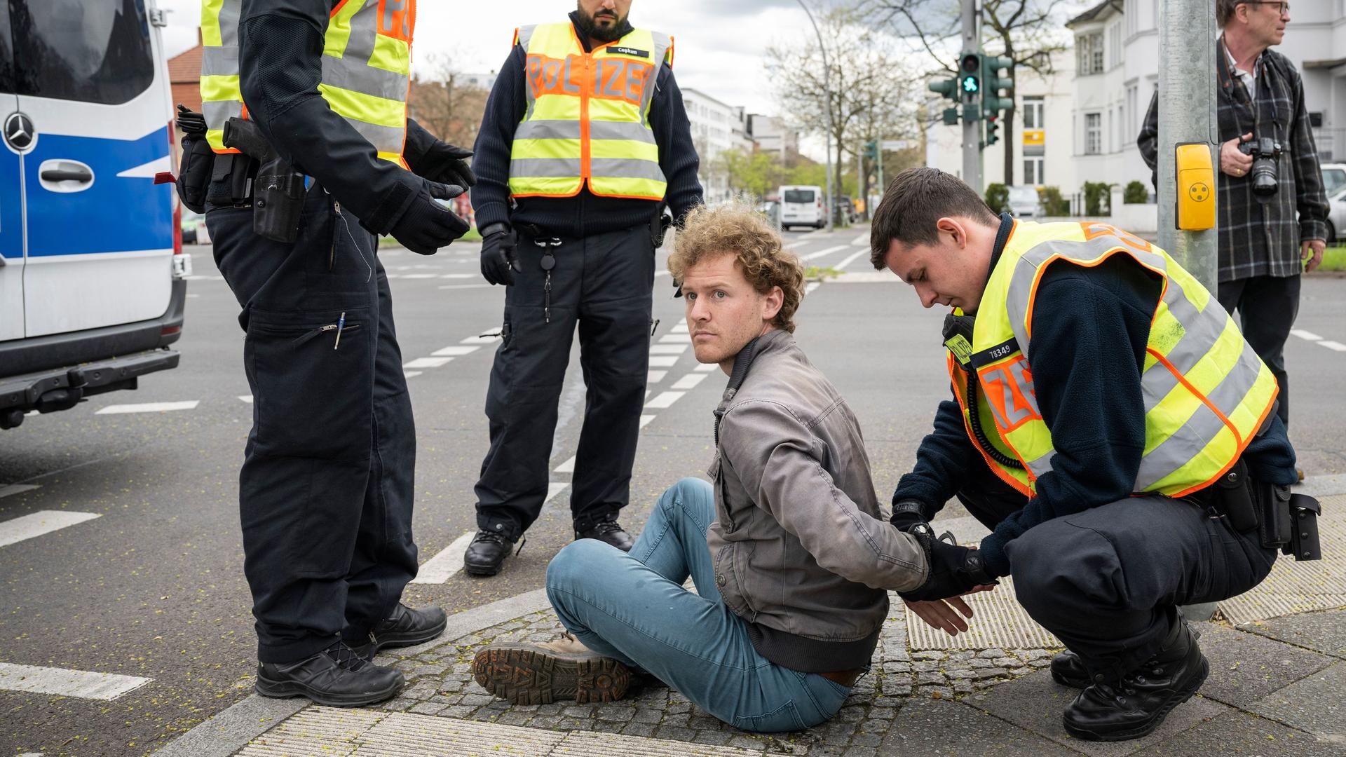 Ein auf der Straße sitzender Aktivist bekommt von einem Polizisten Handschellen angelegt. Daneben stehen zwei weitere Polizisten.