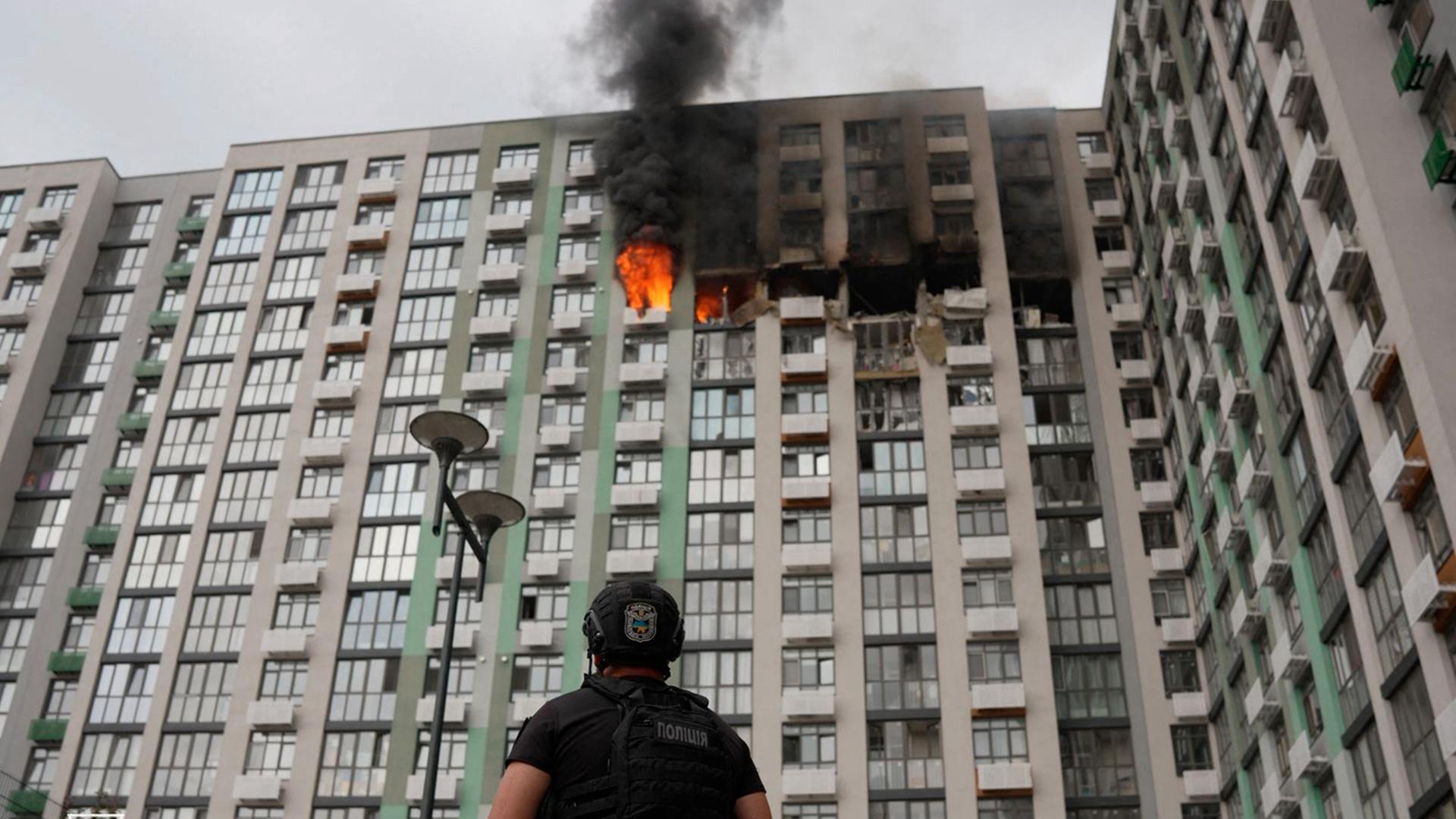 Ein Polizeibeamter in Kiew blickt von unten auf eine brennende Etage in einem Wohnhaus nach einem russischen Angriff in der Ukraine. Ein Polizeibeamter in Kiew blickt von unten auf eine brennende Etage in einem Wohnhaus nach einem russischen Angriff in der Ukraine.