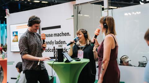 Auf einer Bühne in einer Messehalle stehen Mike Herbstreuth, Maria Lorenz-Bokelberg und Carina Schroeder in gelöster Gesprächshaltung.