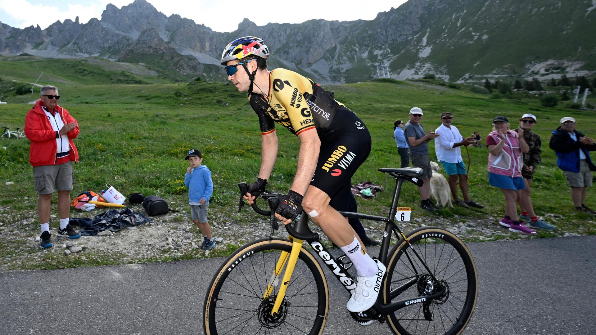Der Radprofi Wout van Aert fährt vor Bergpanorama an Fans vorbei. Der Radprofi Wout van Aert fährt vor Bergpanorama an Fans vorbei.