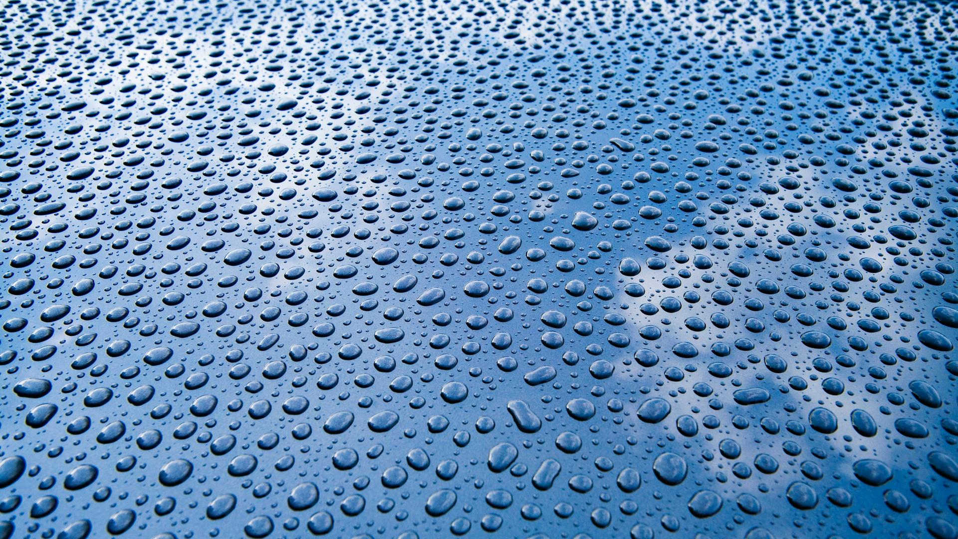 Abperlende Wassertropfen auf einer hellblauen Autokarosserie.