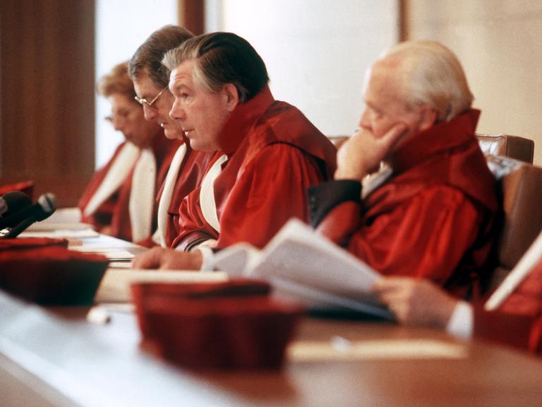 Bundesverfassungsrichter in roten Roben sitzen auf dem Podium. Einer von ihnen spricht in ein Mikrofon.