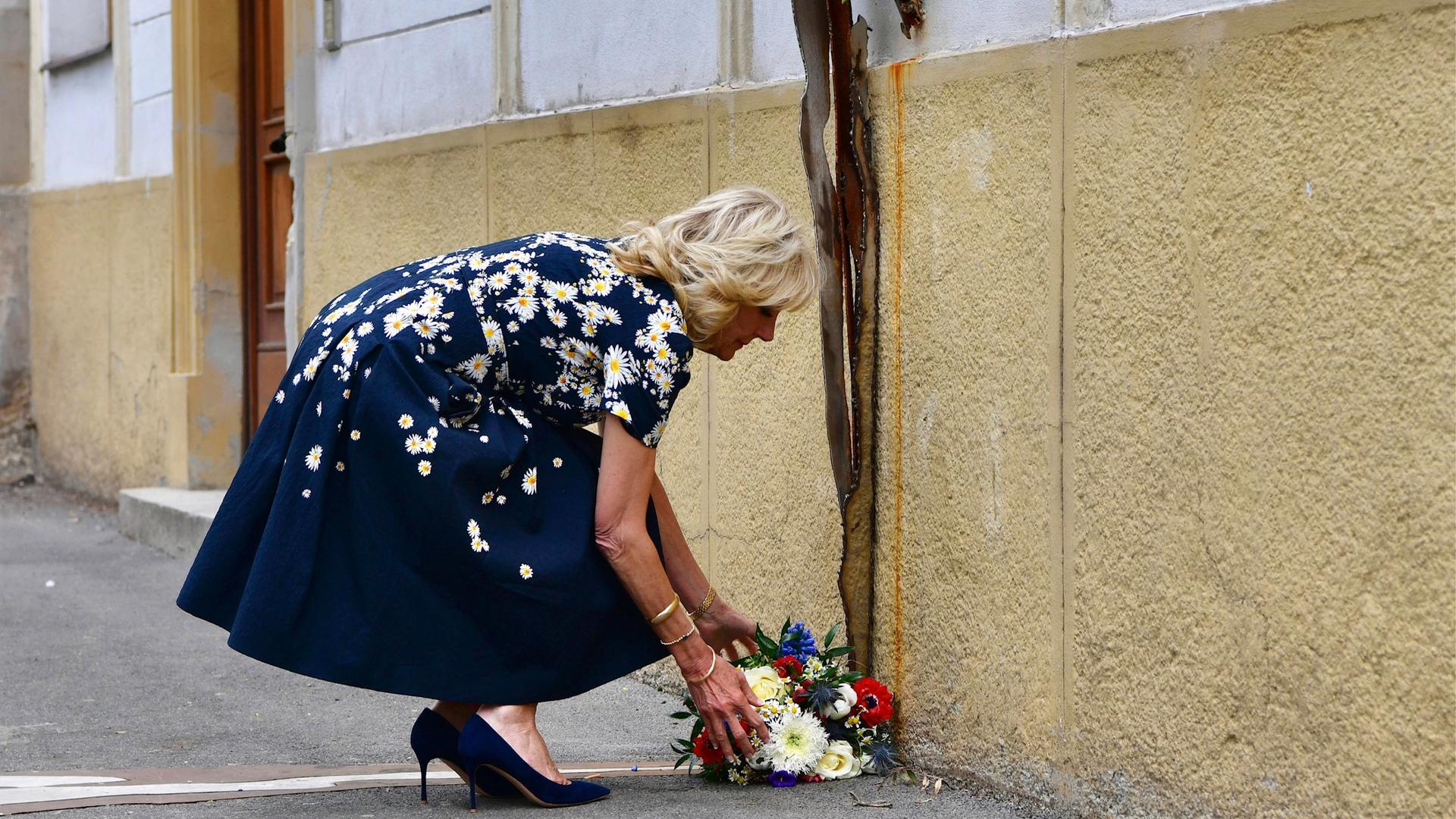 Jill Biden legt vor einem Gebäude einen Kranz ab und kniet nieder dabei