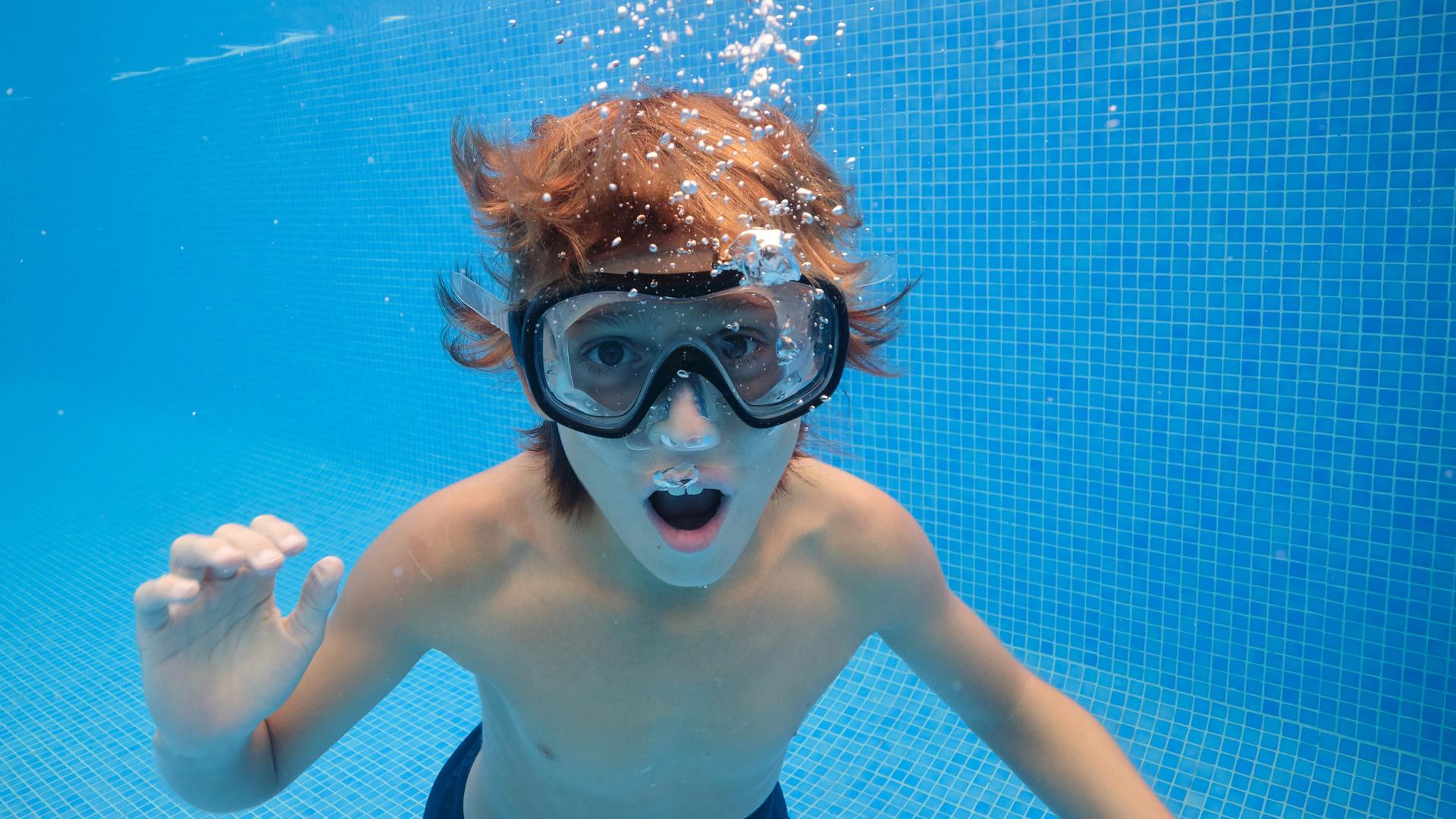 Ein Junge mit Taucherbrille unter Wasser im Pool