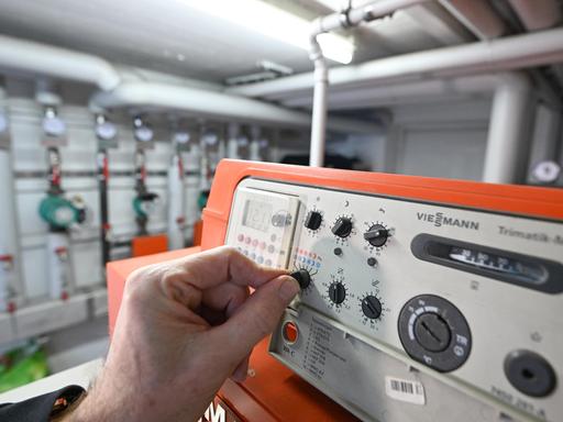 Eine Hand reguliert die Steuerungsanlage einer Gasheizung in einem Mehrfamilienhaus. 