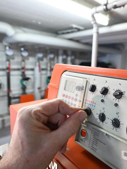 Eine Hand reguliert die Steuerungsanlage einer Gasheizung in einem Mehrfamilienhaus. 