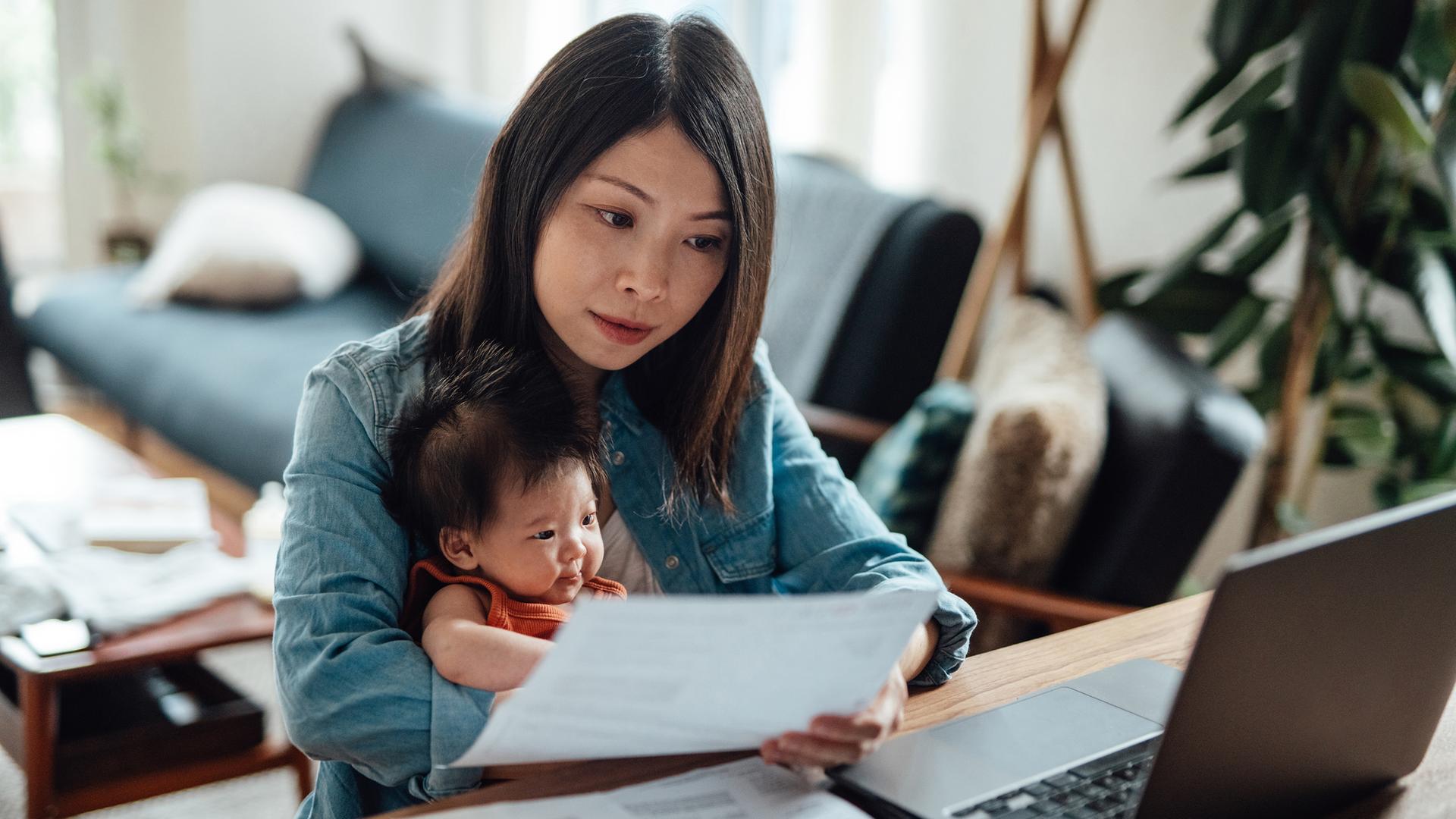 Eine junge Mutter am Laptop mit ihrem Baby auf dem Arm. Eine junge Mutter am Laptop mit ihrem Baby auf dem Arm.