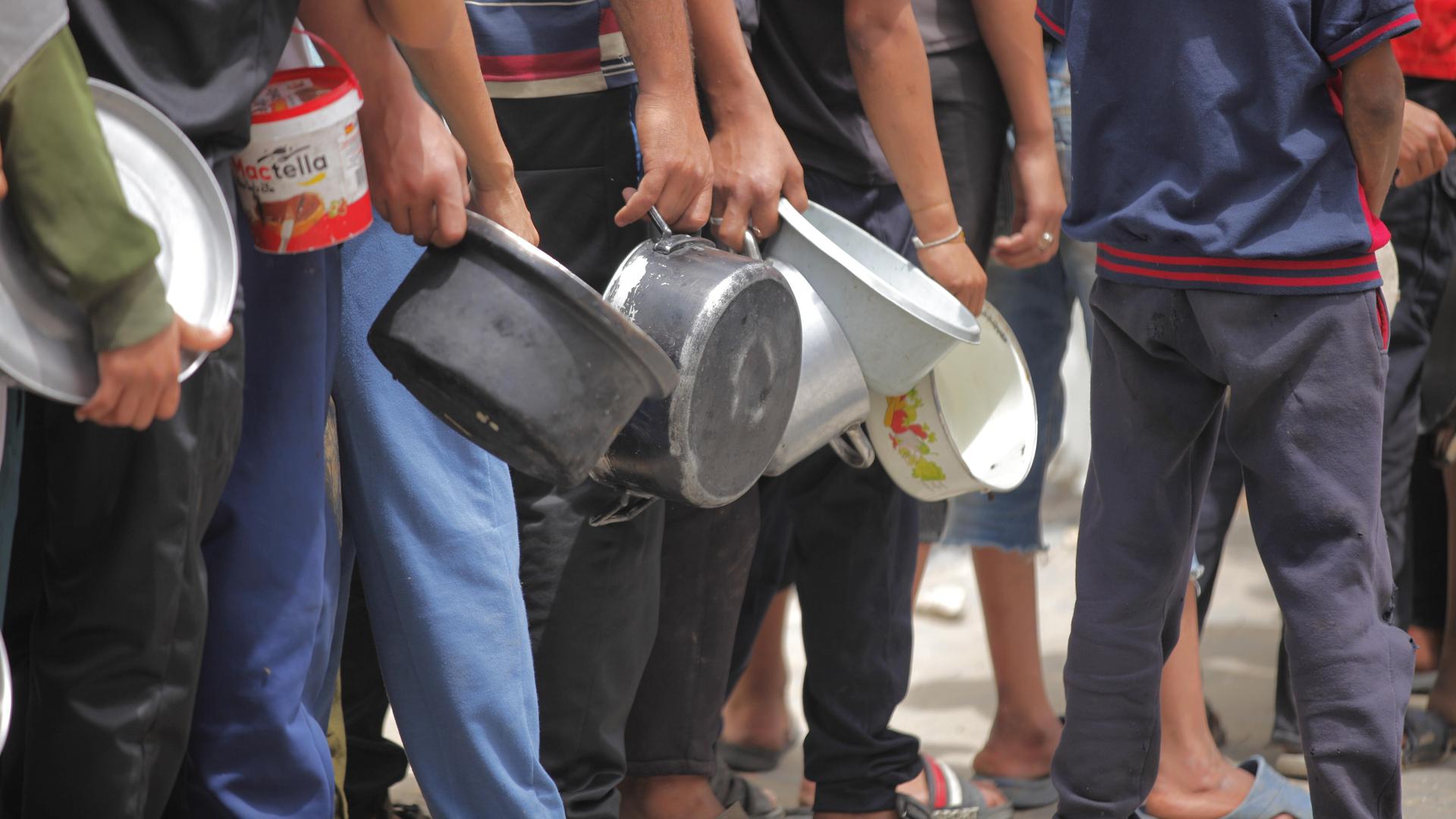 Menschen aus dem Gazastreifen stehen am 12. Mai 2025 vor einer Essensausgabe und haben leere Töpfe in der Hand