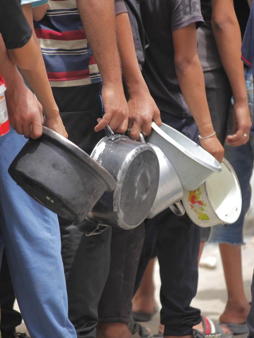 Menschen aus dem Gazastreifen stehen am 12. Mai 2025 vor einer Essensausgabe und haben leere Töpfe in der Hand