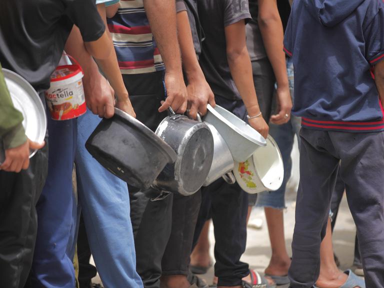 Menschen aus dem Gazastreifen stehen am 12. Mai 2025 vor einer Essensausgabe und haben leere Töpfe in der Hand