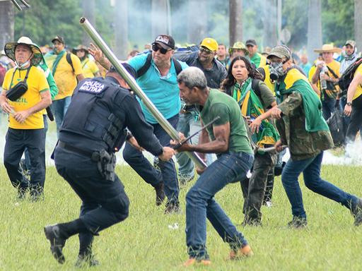 Ein Mann schlägt einen Polizisten mit einer Stange. Dahinter stürmen viele weitere Bolsonaro-Anhänger heran.