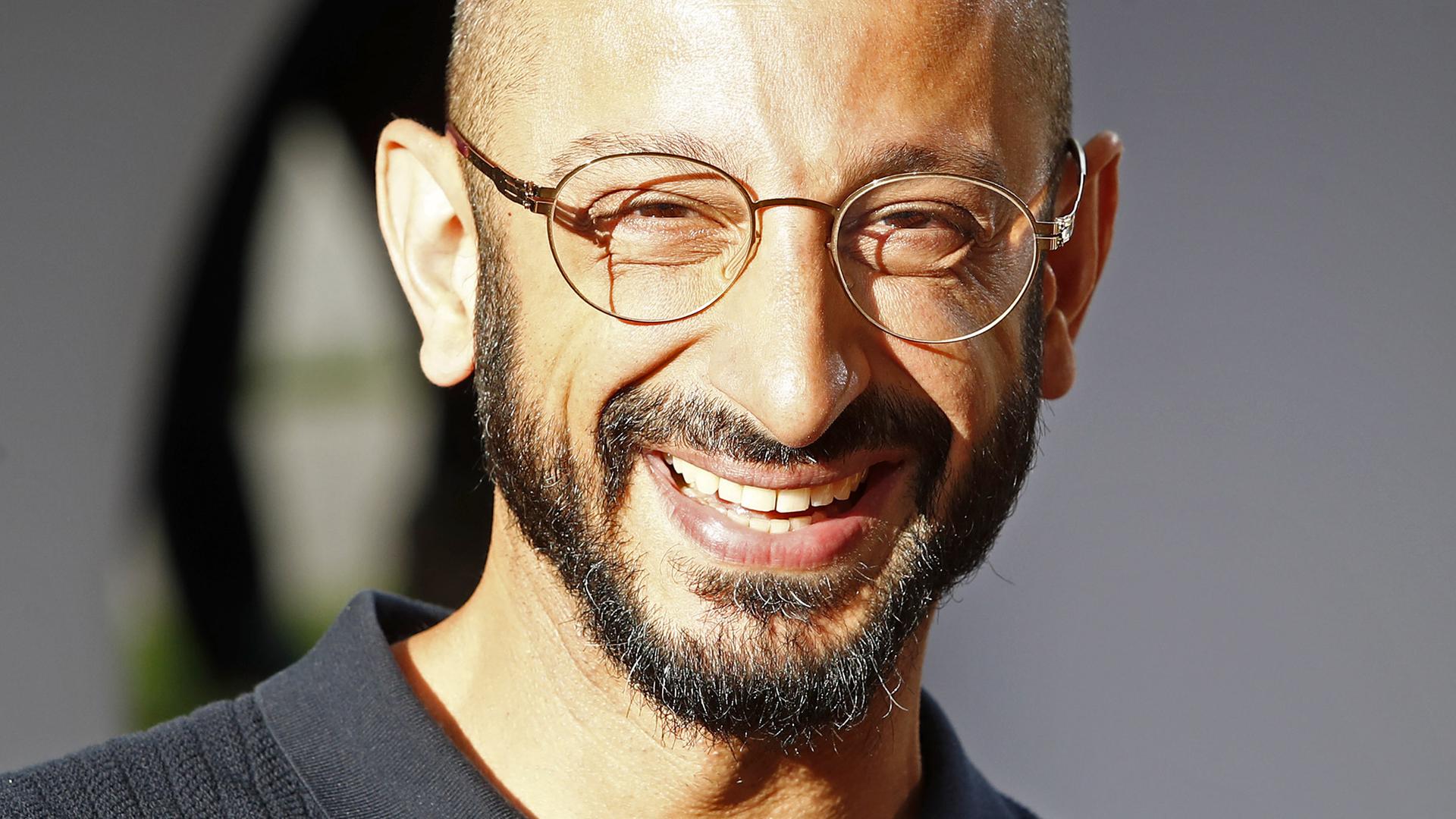 Behzad Karim Khani lacht in die Kamera. Er hat eine Glatze, einen kurzen Vollbart und trägt eine Brille mit dünnem Rand.