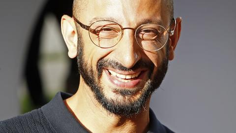 Behzad Karim Khani lacht in die Kamera. Er hat eine Glatze, einen kurzen Vollbart und trägt eine Brille mit dünnem Rand.