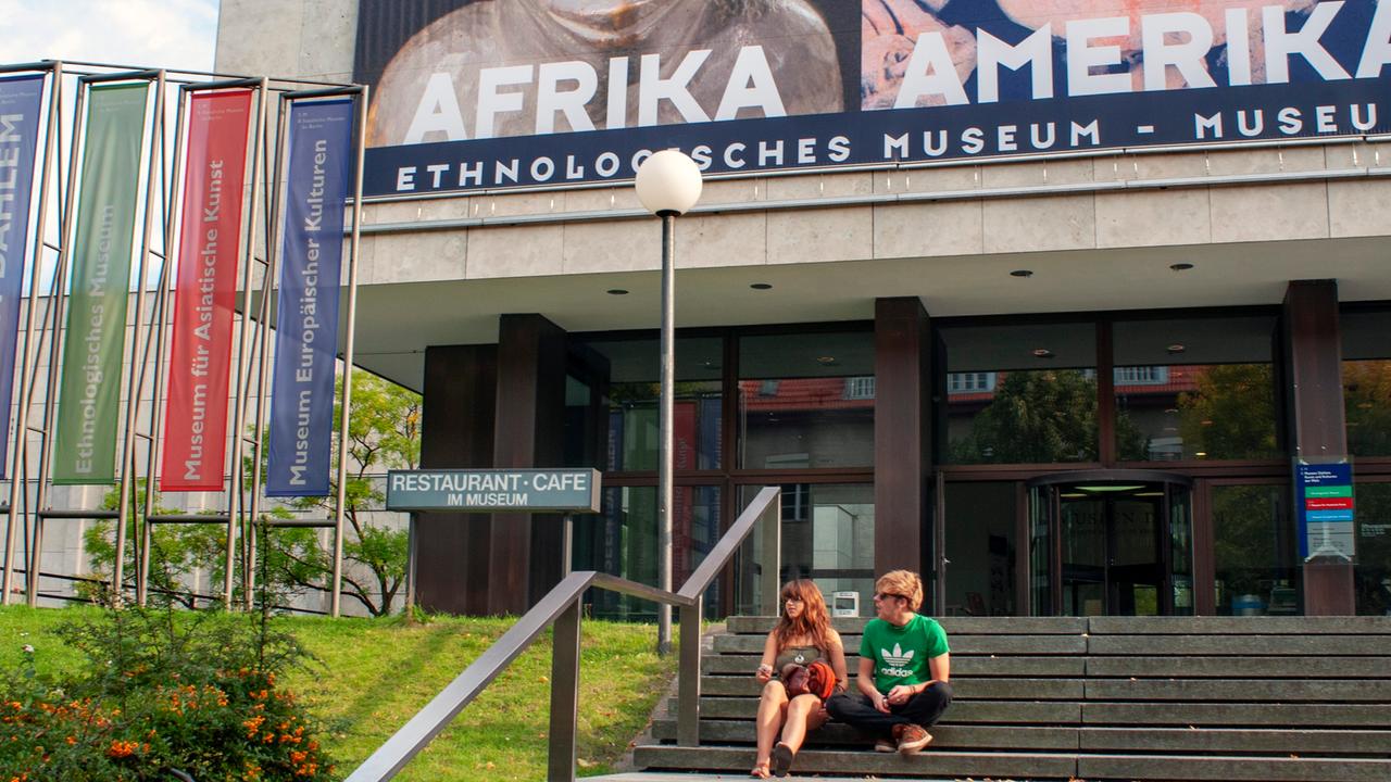 Ein Mann und eine Frau sitzen auf einer Freitreppe vor einem Museumseingang.