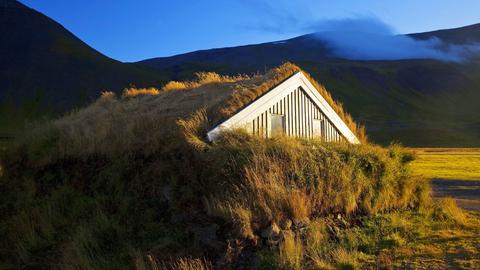 Ein Holzhaus mit Grassodendach in Island im Abendlicht.