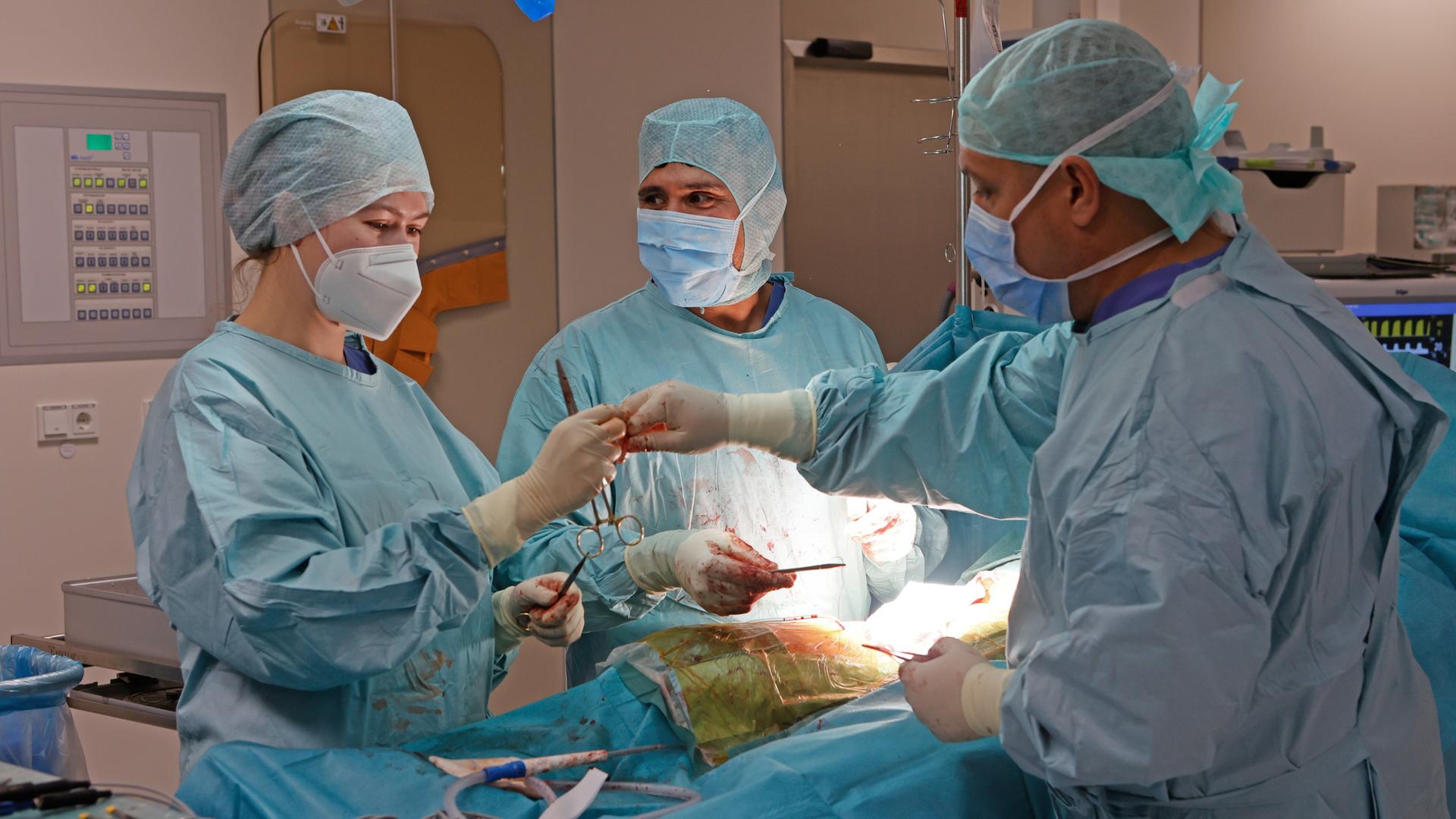 Eine Ärztin und 2 Ärzte operieren einen Patienten. 
