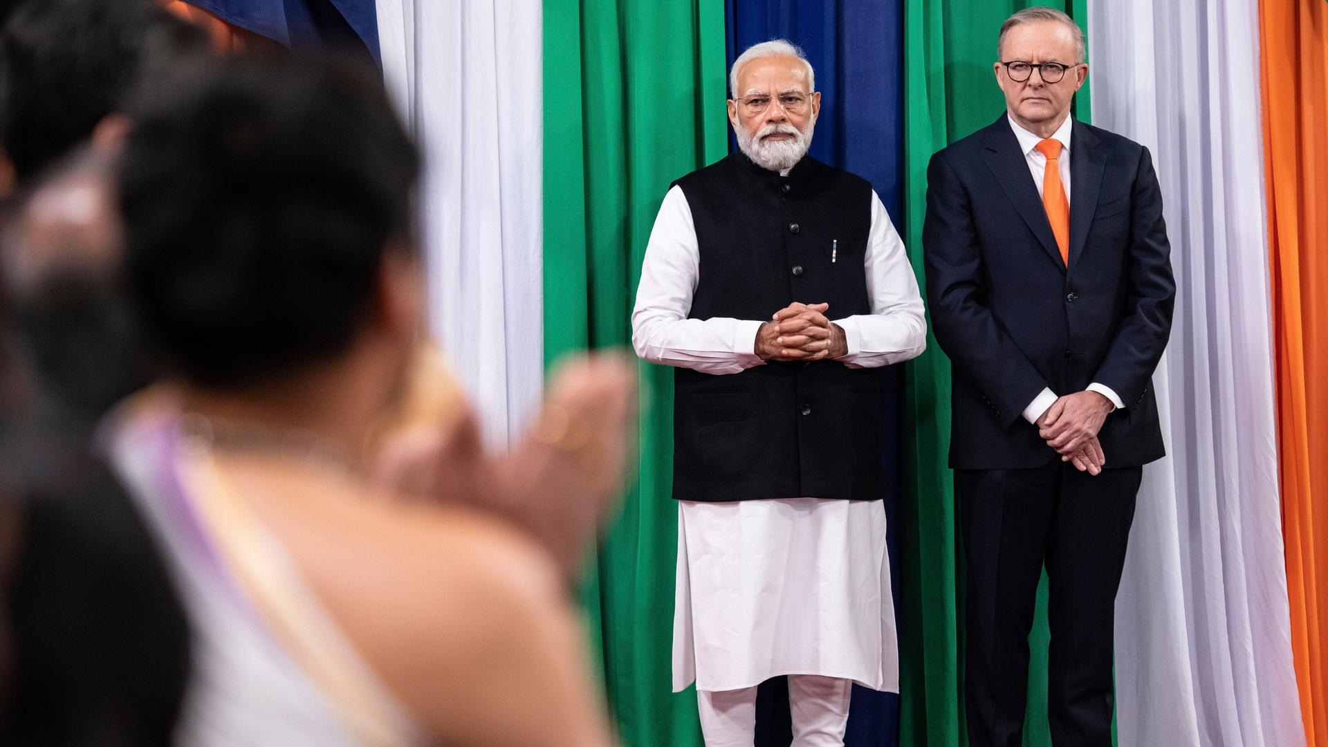 Der indische Premierminister Modi steht mit seinem australischen Kollegen Albanese auf einer Bühne. Im Vordergrund stehen verschwommen Menschen und klatschen. Der indische Premierminister Modi steht mit seinem australischen Kollegen Albanese auf einer Bühne. Im Vordergrund stehen verschwommen Menschen und klatschen.