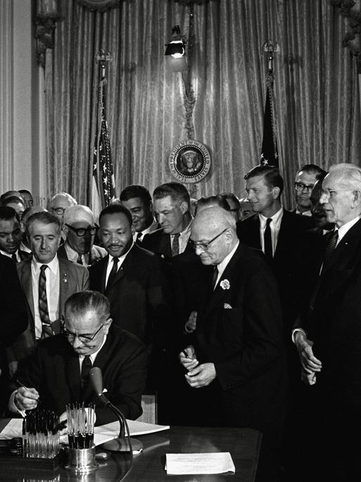 US-Präsident Lyndon Baines Johnson unterzeichnet das Bürgerrechtsgesetz (Civil Rights Act) von 1964, hinter dem Präsidenten steht Bürgerrechtler Martin Luther King