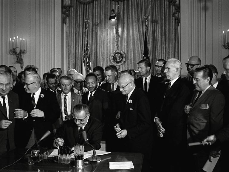 US-Präsident Lyndon Baines Johnson unterzeichnet das Bürgerrechtsgesetz (Civil Rights Act) von 1964, hinter dem Präsidenten steht Bürgerrechtler Martin Luther King