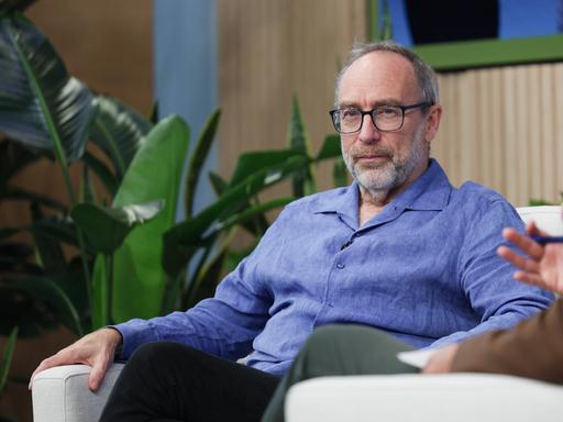 Jimmy Wales sitzt auf einer Bühne auf einem Sessel 