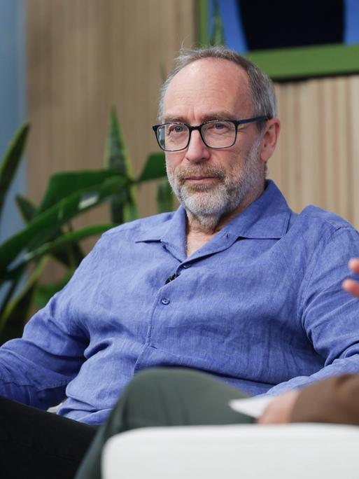 Jimmy Wales sitzt auf einer Bühne auf einem Sessel 