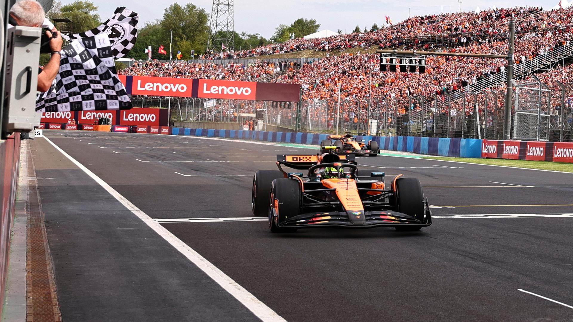 Das Bild zeigt den gelben Formel-1-Rennwagen beim Überqueren der Ziellinie. Im Hintergrund eine vollbesetzte Tribüne.