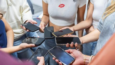 Jugendliche halten viele Mobiltelefone in der Hand, bilden mit ihren Händen einen Kreis.
