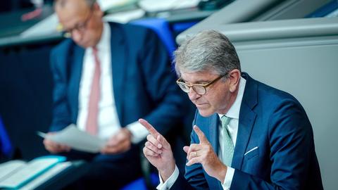 Wolfgang Weimer, Kulturstaatsminister, spricht in der Generaldebatte des Bundestags. Er hält die beiden Zeigefinger vor sich. Im Hintergrund ist verschwommen Friedrich Merz.