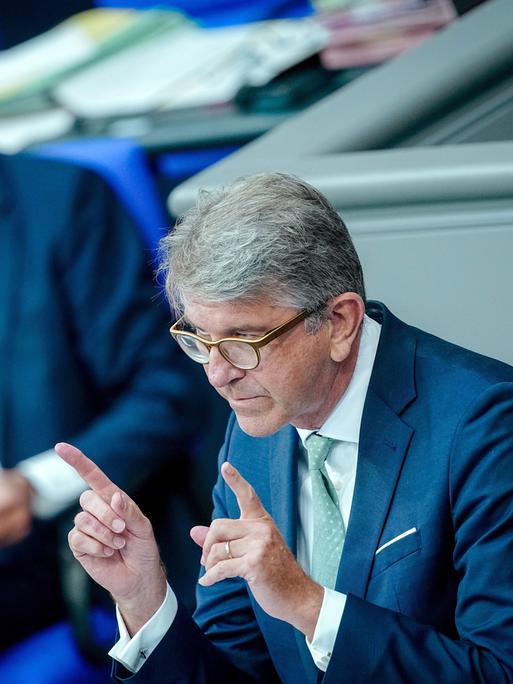 Wolfgang Weimer, Kulturstaatsminister, spricht in der Generaldebatte des Bundestags. Er hält die beiden Zeigefinger vor sich. Im Hintergrund ist verschwommen Friedrich Merz.