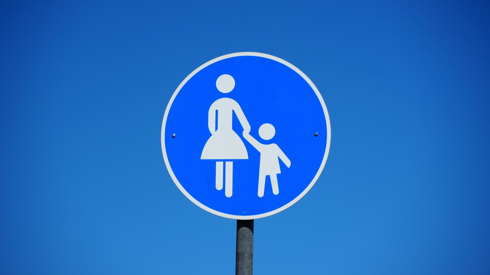 Blaues rundes Verkehrsschild mit einer Frau die ein Kind an der Hand hält als Hinweisschild für einen Gehweg