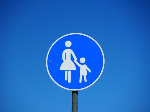 Blaues rundes Verkehrsschild mit einer Frau die ein Kind an der Hand hält als Hinweisschild für einen Gehweg
