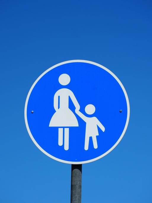 Blaues rundes Verkehrsschild mit einer Frau die ein Kind an der Hand hält als Hinweisschild für einen Gehweg