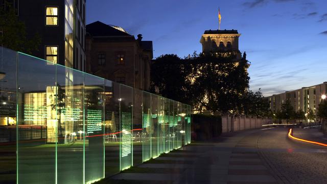 Beleuchtete Glastafaln mit den Artikeln aus dem Grundgesetz im Regierungsviertel in Berlin. Im Hintergrund ist der Reichstag zu sehen.
